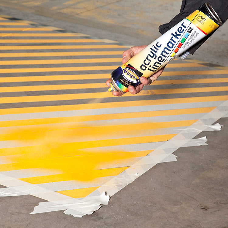 Yellow line-marking paint being sprayed through a floor stencil