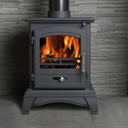 Black freestanding stove with flames inside, against a gray tiled wall.