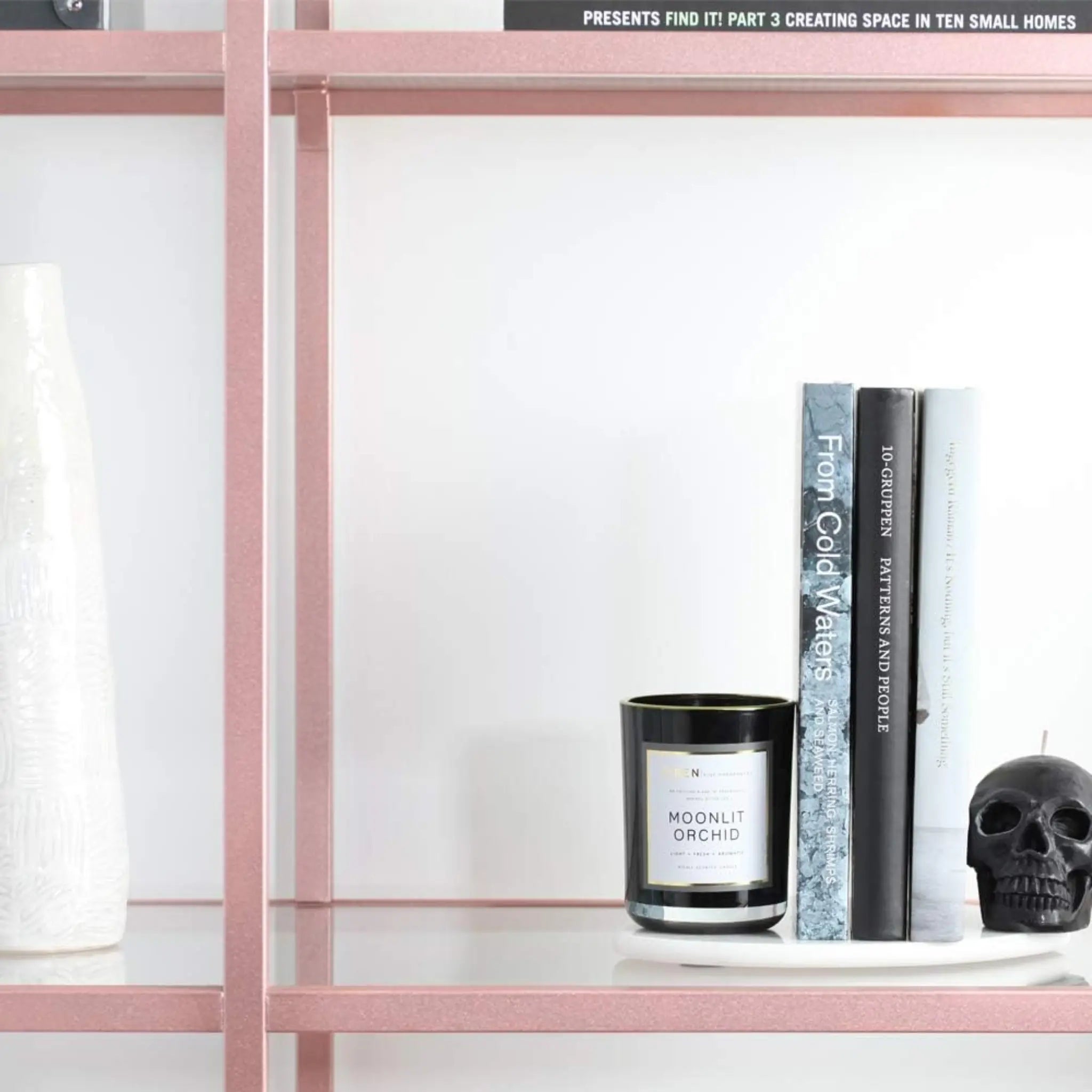 Pink shelf with a candle, books, and a skull decoration against a white background