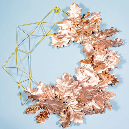 Decorative wall art with rose gold leaves and geometric gold frame on a light blue background