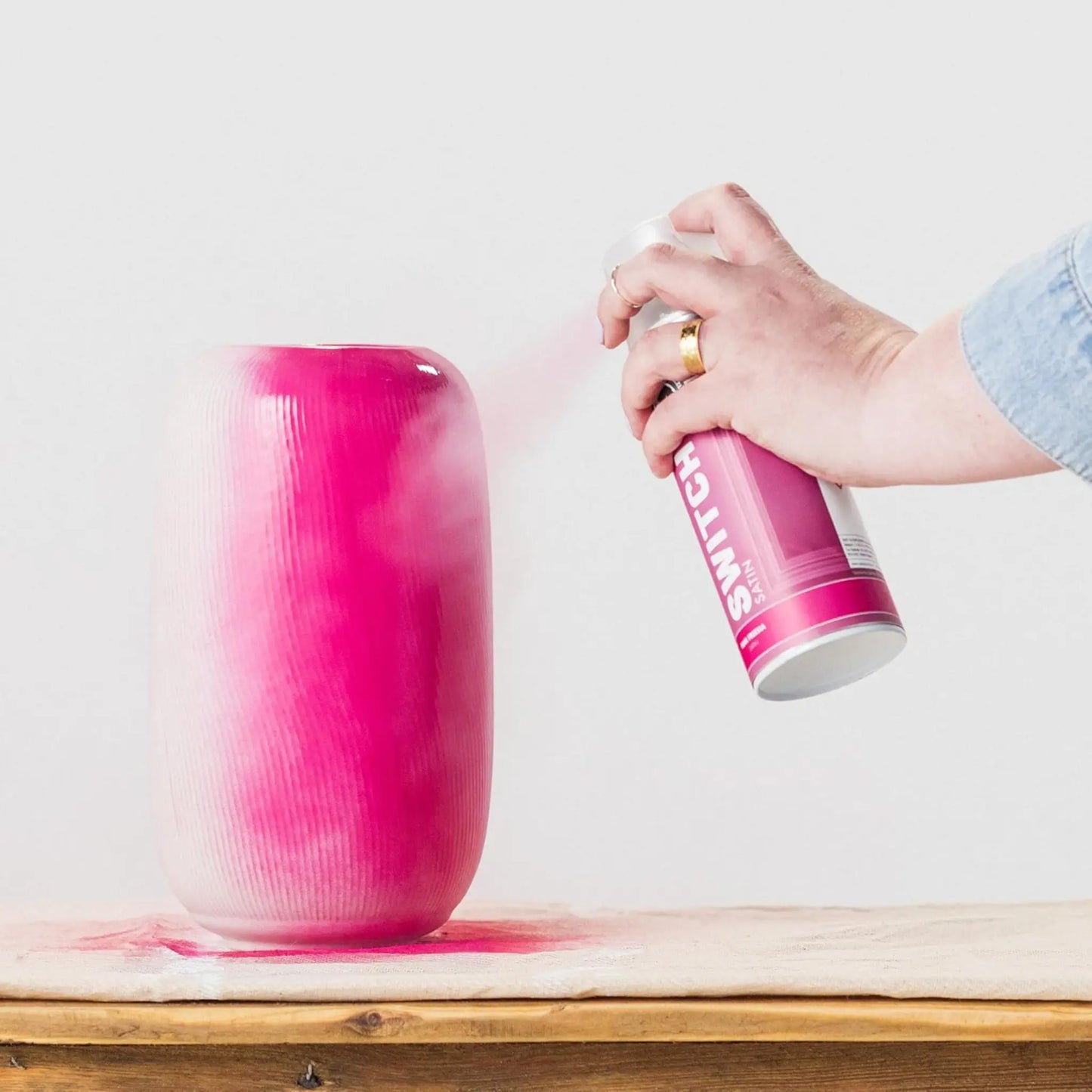 Person spraying pink paint onto a textured vase with a can labeled 'Rollins' on a light background.