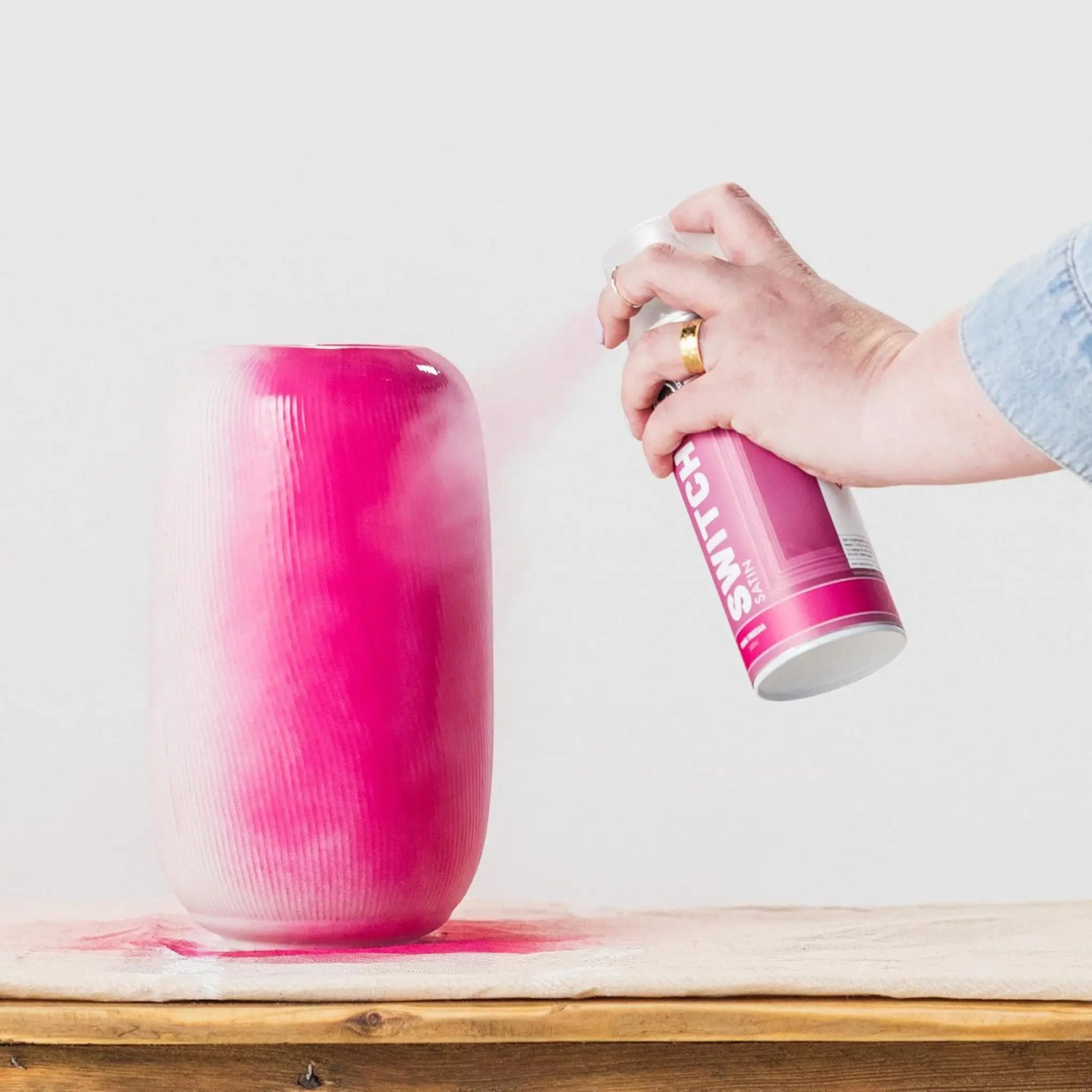 Person spraying pink paint onto a textured vase with a can labeled 'Rollins' on a light background.