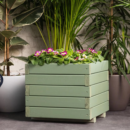 Green wooden planter with flowers against a neutral background